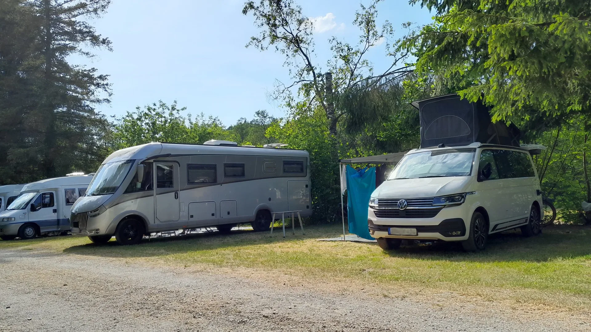 Campingbusse und Wohnwagen auf dem begrünten Campingplatz.