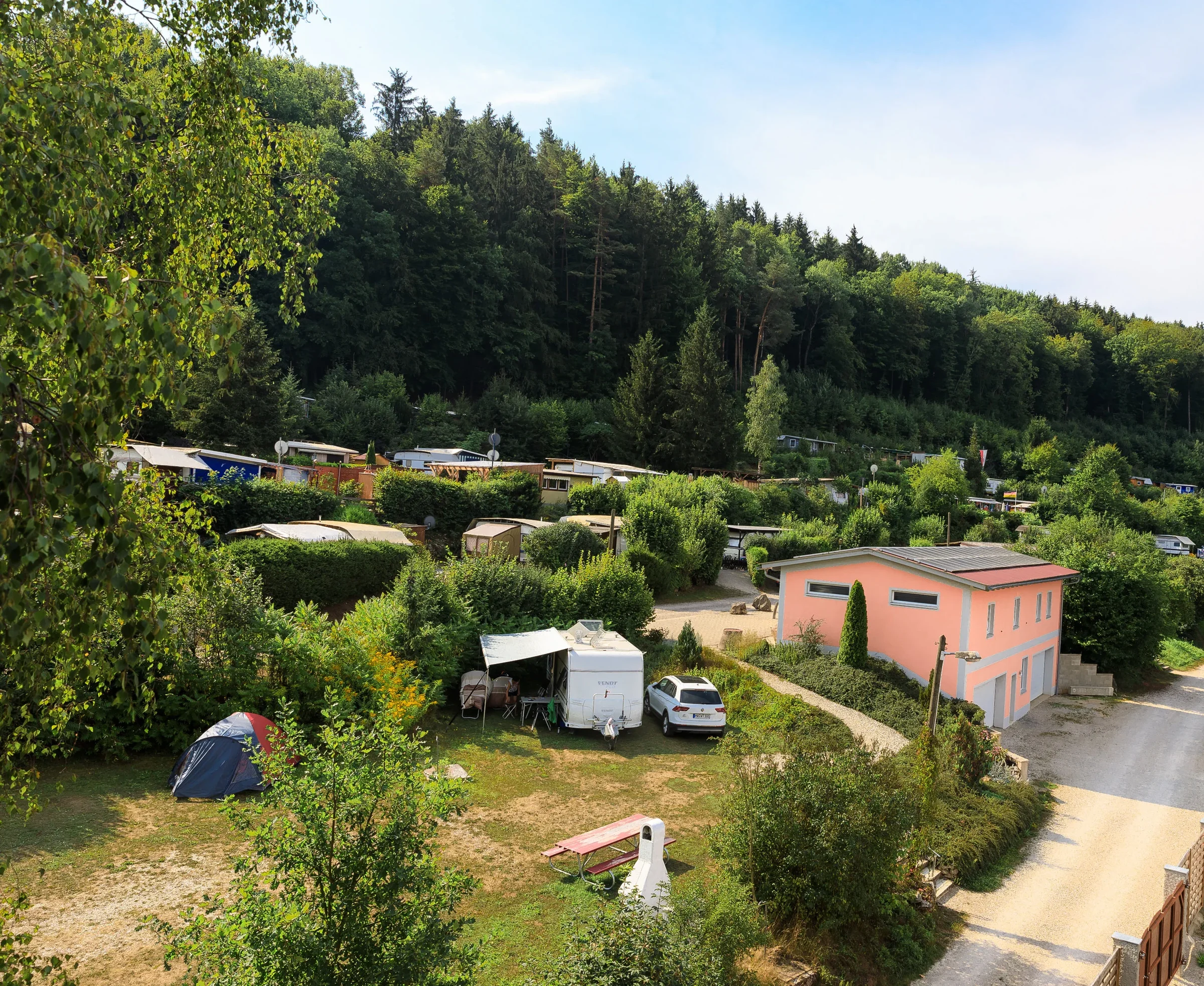 Blick über den Campingplatz mit Stellplätzen und bewaldetem Hang.