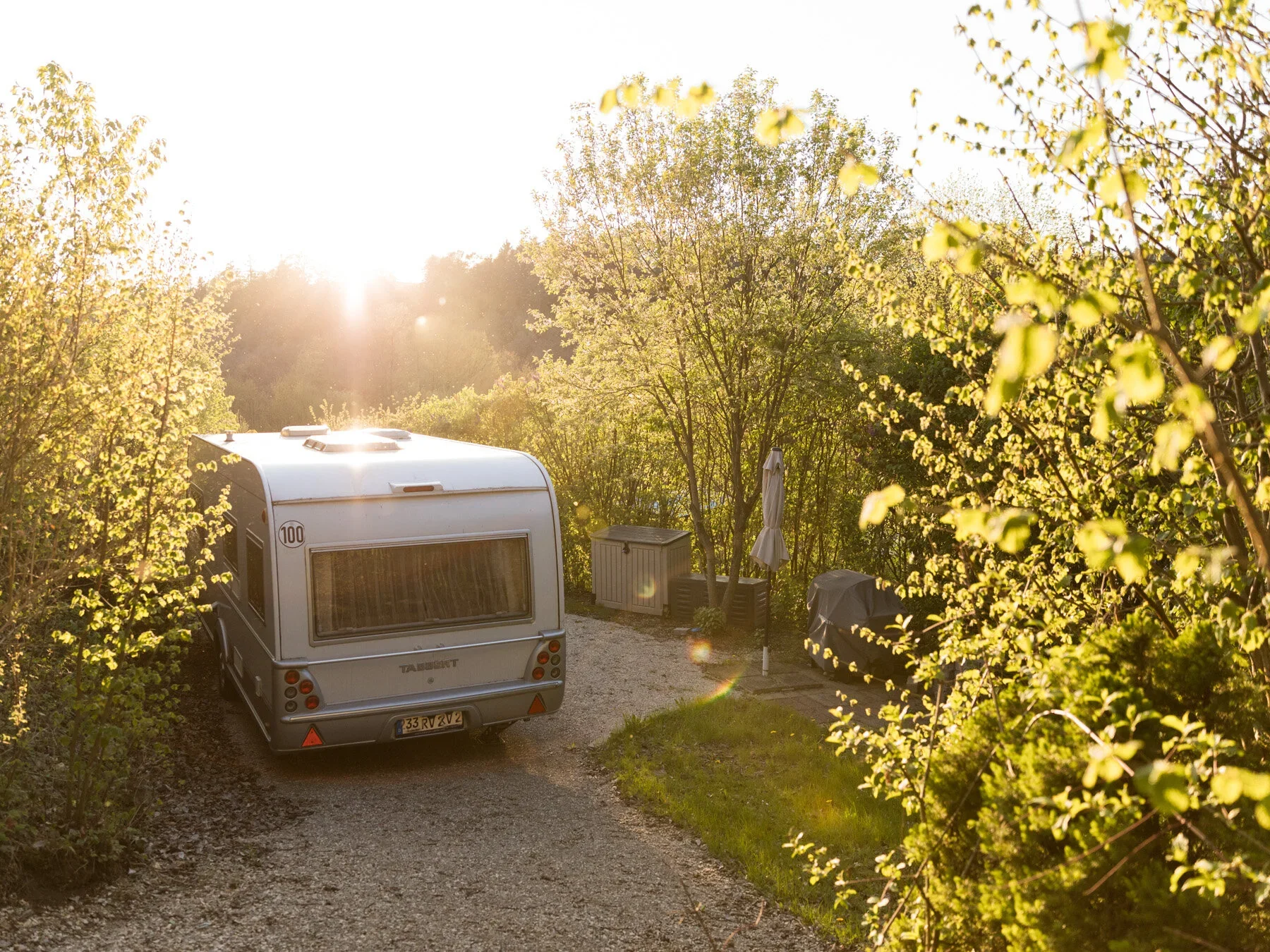 Wohnwagen hinter einer Hecke im warmen Sonnenlicht.