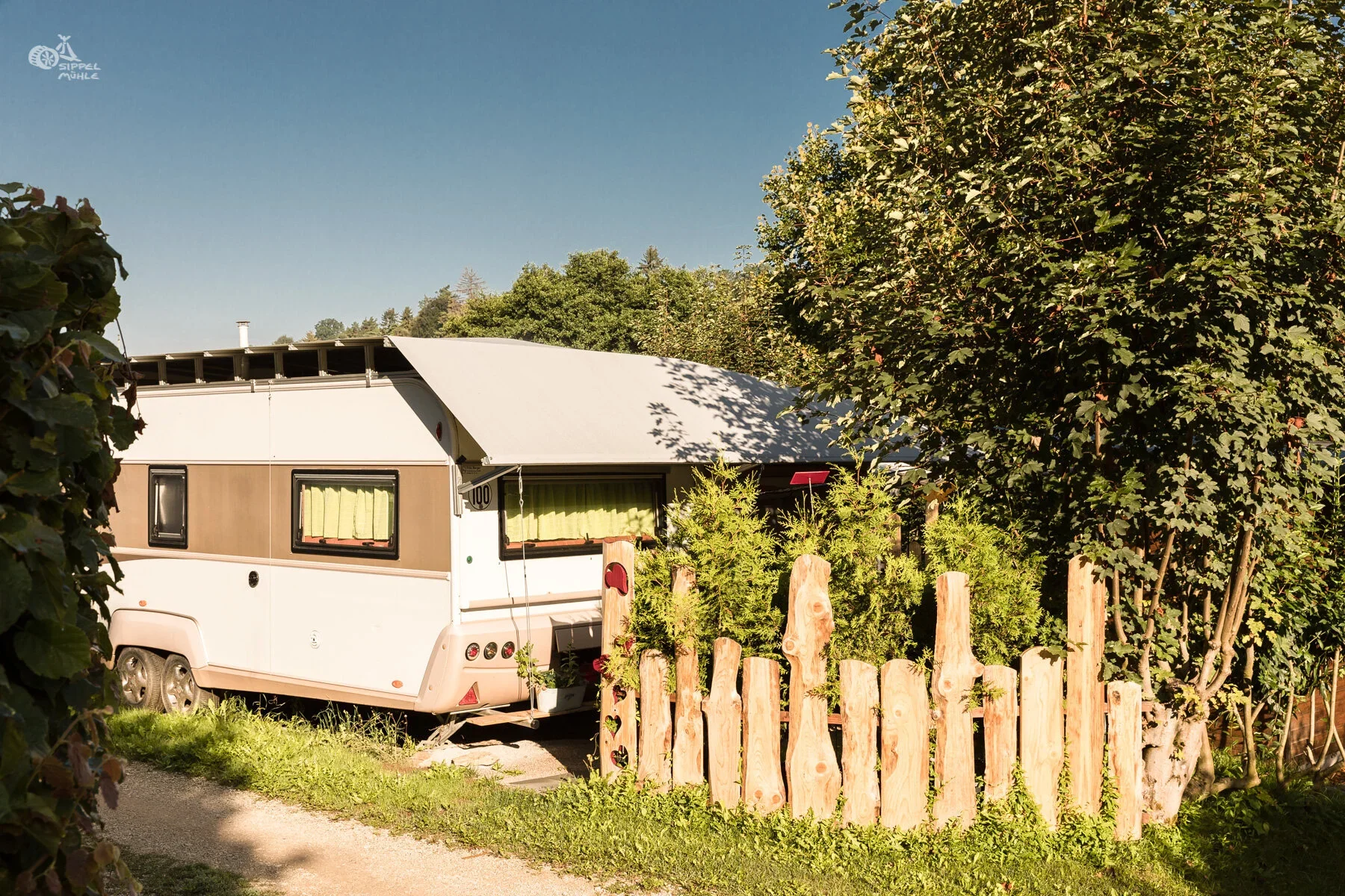 Wohnwagen mit bepflanztem Vorgarten und niedrigem Holzzaun.