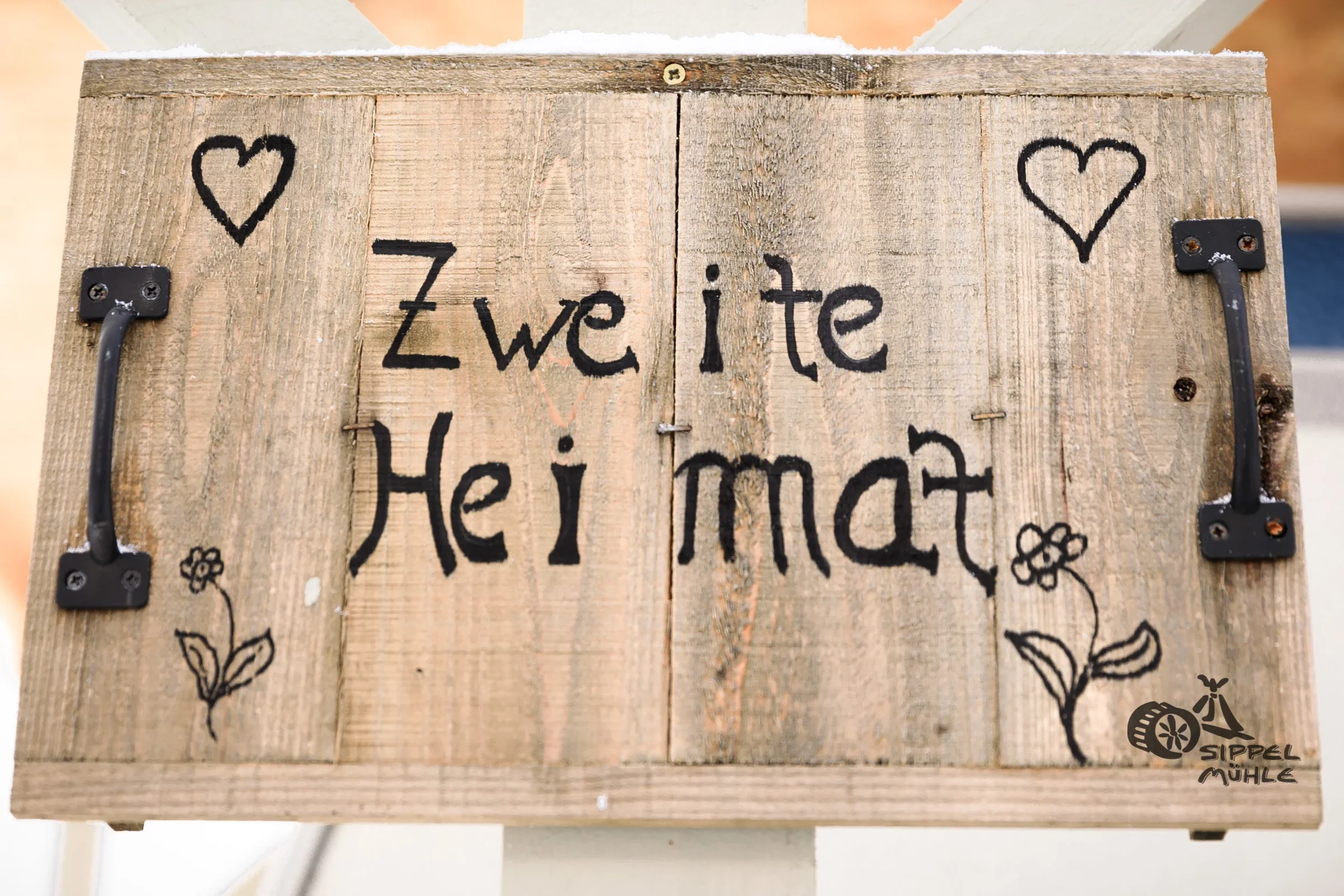 Holzschild mit Herzmotiven und dem Schriftzug Zweite Heimat.