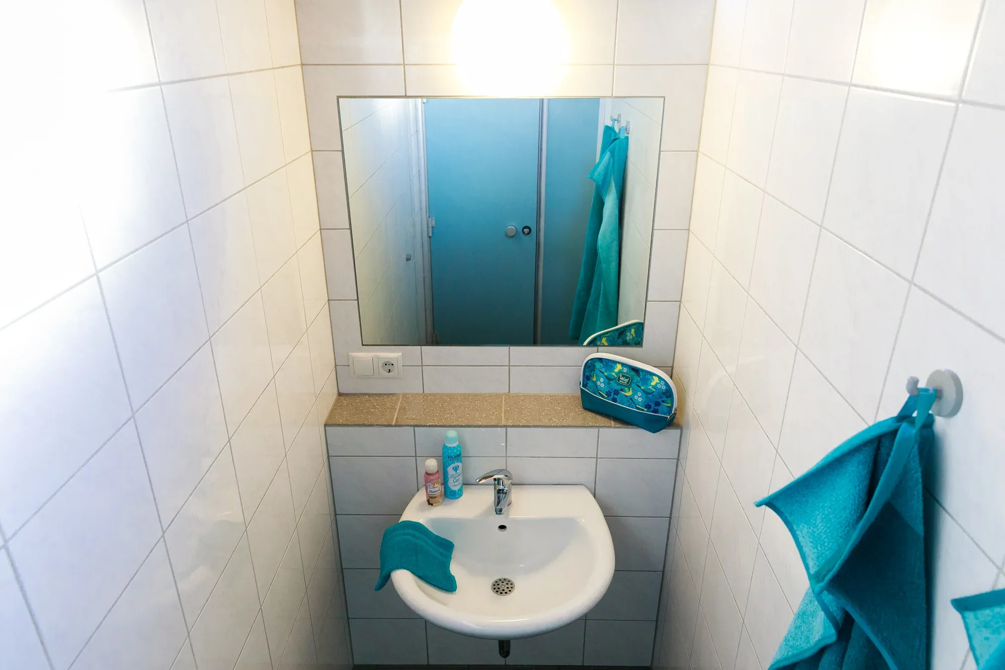 Einzelwaschkabine mit Waschbecken, Spiegel und türkisfarbenem Handtuch.