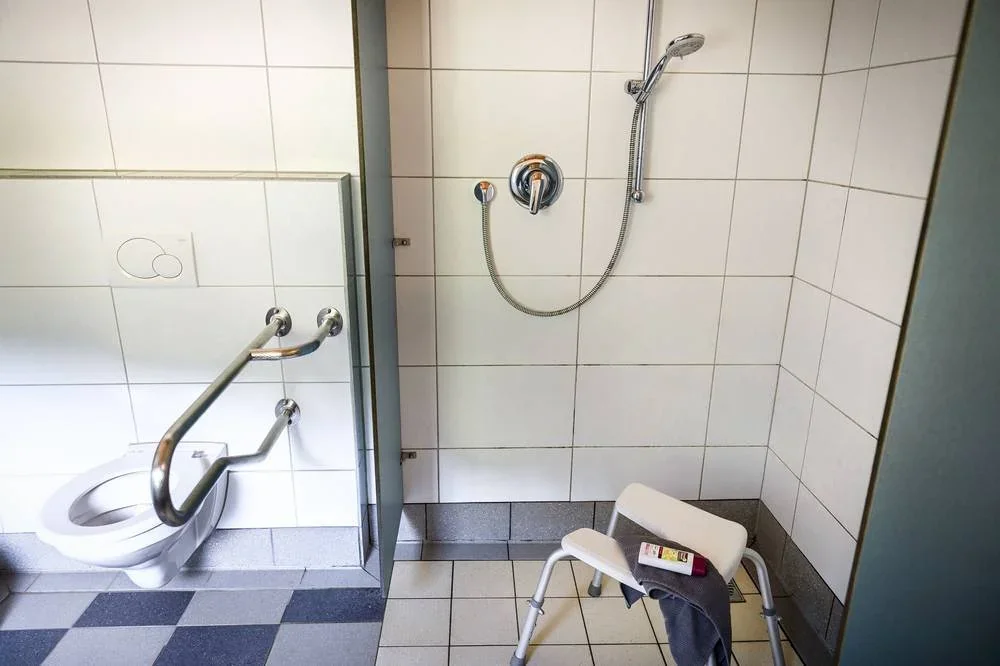 WC mit Haltegriff und Dusche im barrierefreien Sanitärraum.