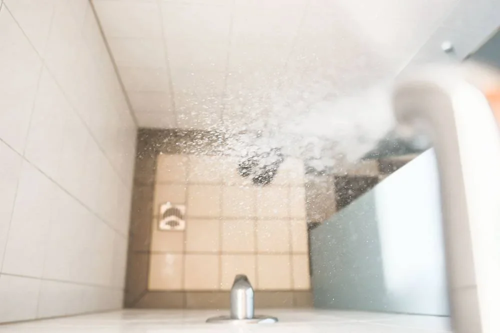 Duschkopf mit fließendem Wasser in einer gefliesten Duschkabine.