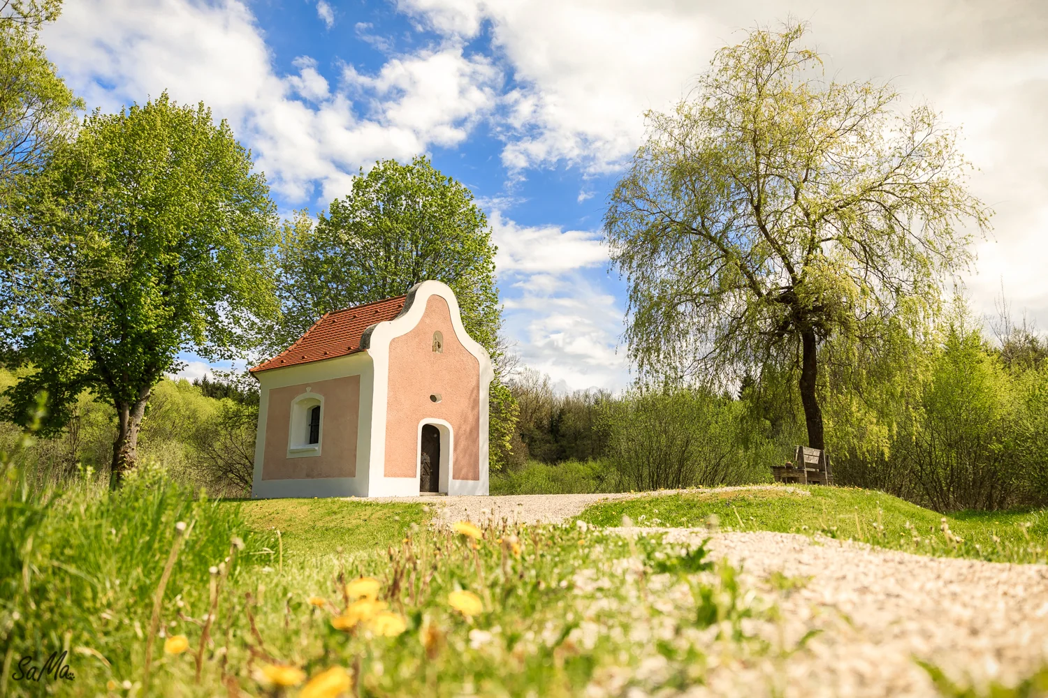 Sonniger Weg zur Ulrichskapelle zwischen Wiesen und Bäumen.