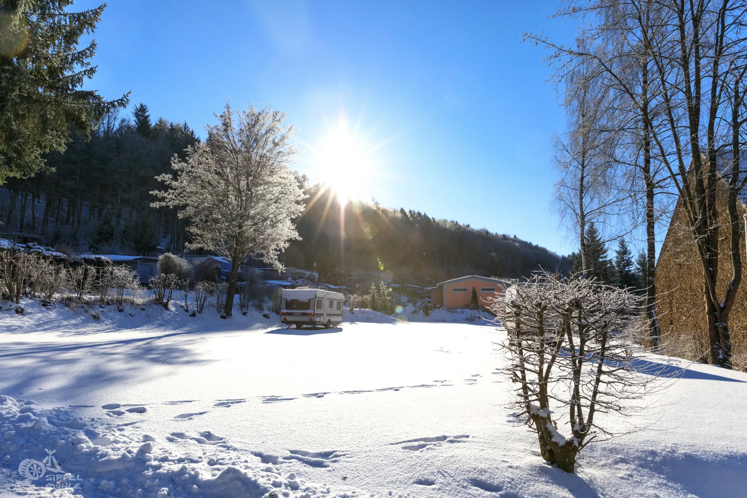 Verschneiter Campingplatz mit Wohnwagen im Winter.